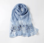 Denim blue silk blend shawl laid flat with blue floral and trailing frond embroidery across both ends