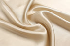 Macro of champagne beige charmeuse swirling into soft folds with a warm satin sheen