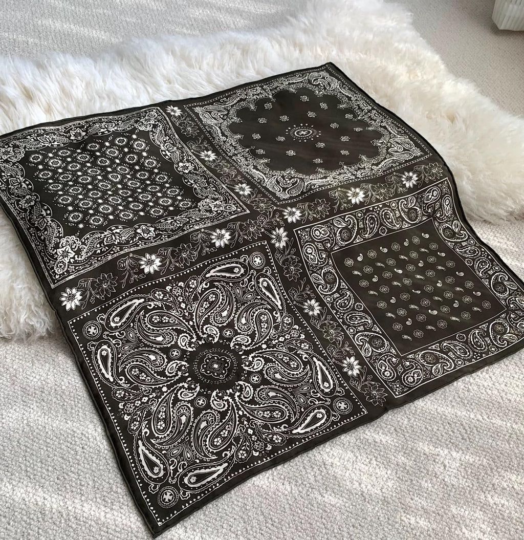 Black bandana square opened flat on a white throw, four paisley corner panels
