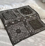 Black bandana square opened flat on a white throw, four paisley corner panels