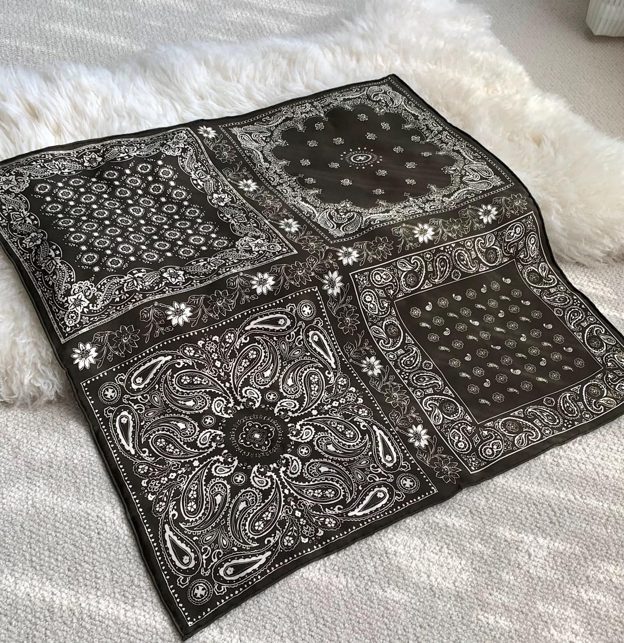 Black bandana square opened flat on a white throw, four paisley corner panels