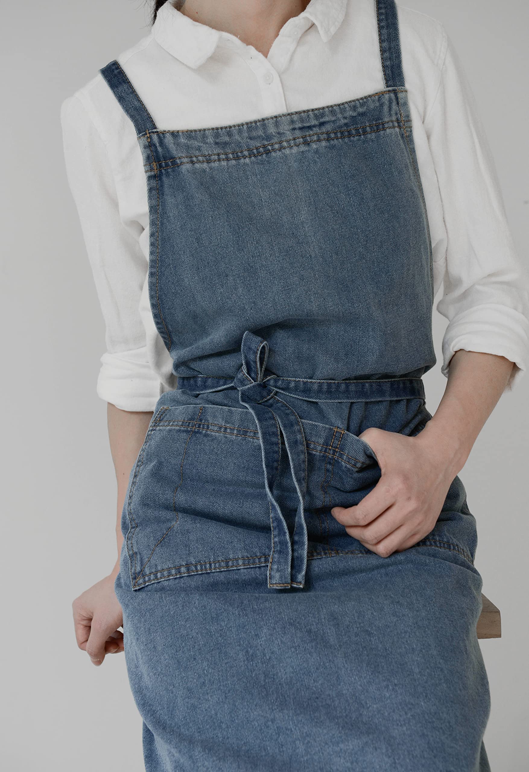 Mid blue denim apron laid flat showing the front pocket and the long shoulder straps