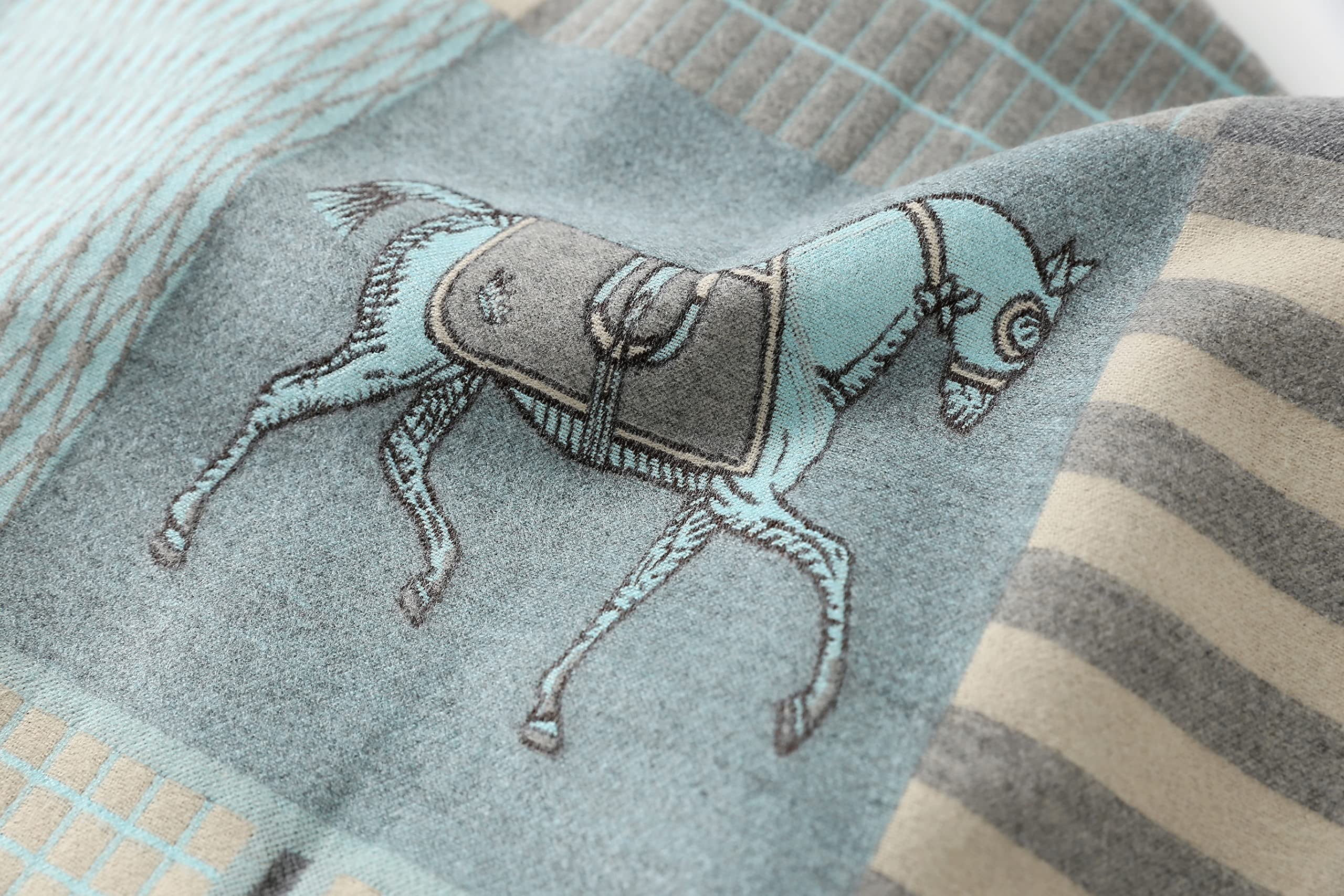 Macro of a single saddled horse motif woven in cream and grey on the pale blue ground