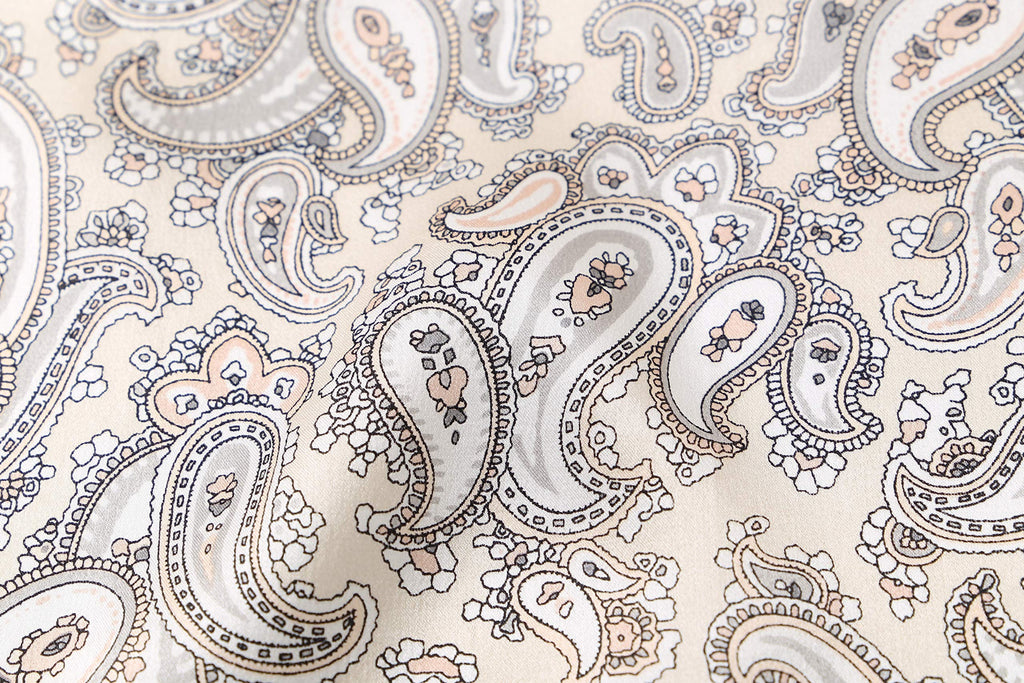 Macro of the print, fine taupe and apricot paisley teardrops on warm cream silk