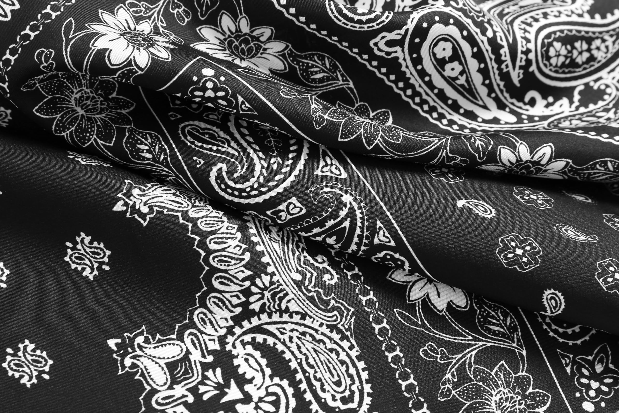 Macro of white paisley and daisy motifs printed on glossy black silk folds