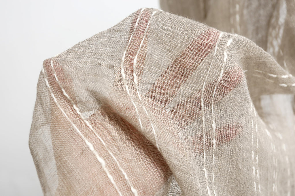 Slub stripe linen scarf held up showing daylight through the loose plain weave
