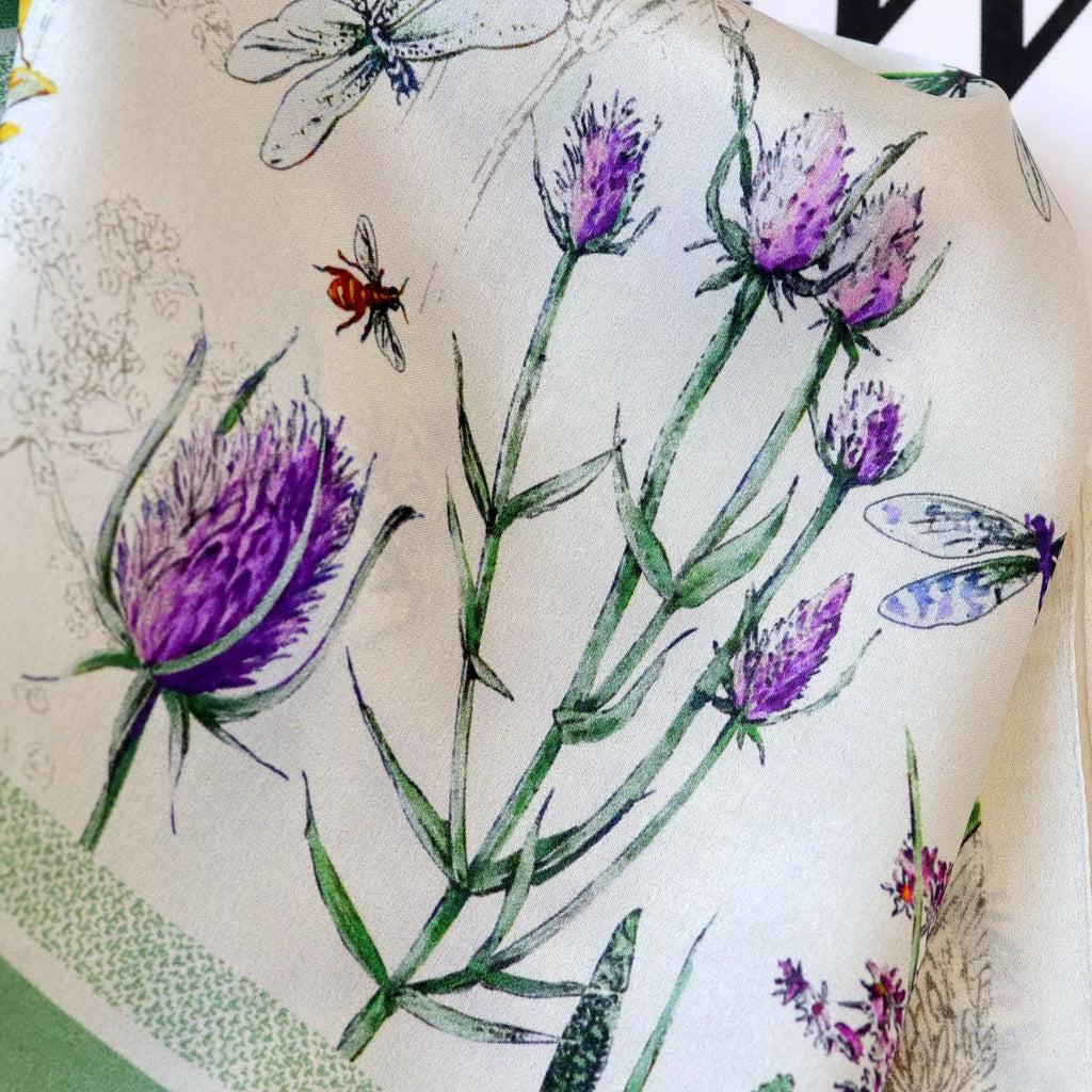 Macro of purple thistles, lavender sprigs and a small bee on ivory charmeuse