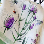 Macro of purple thistles, lavender sprigs and a small bee on ivory charmeuse