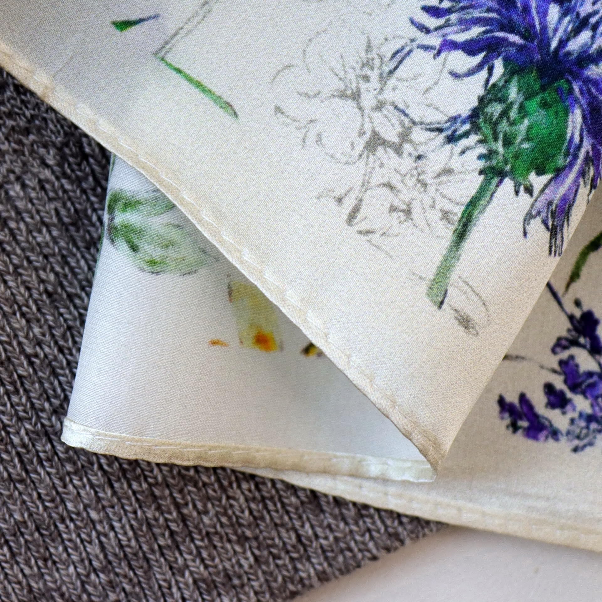 Folded corner of the ivory square over a brown knit, cornflower and rolled hem